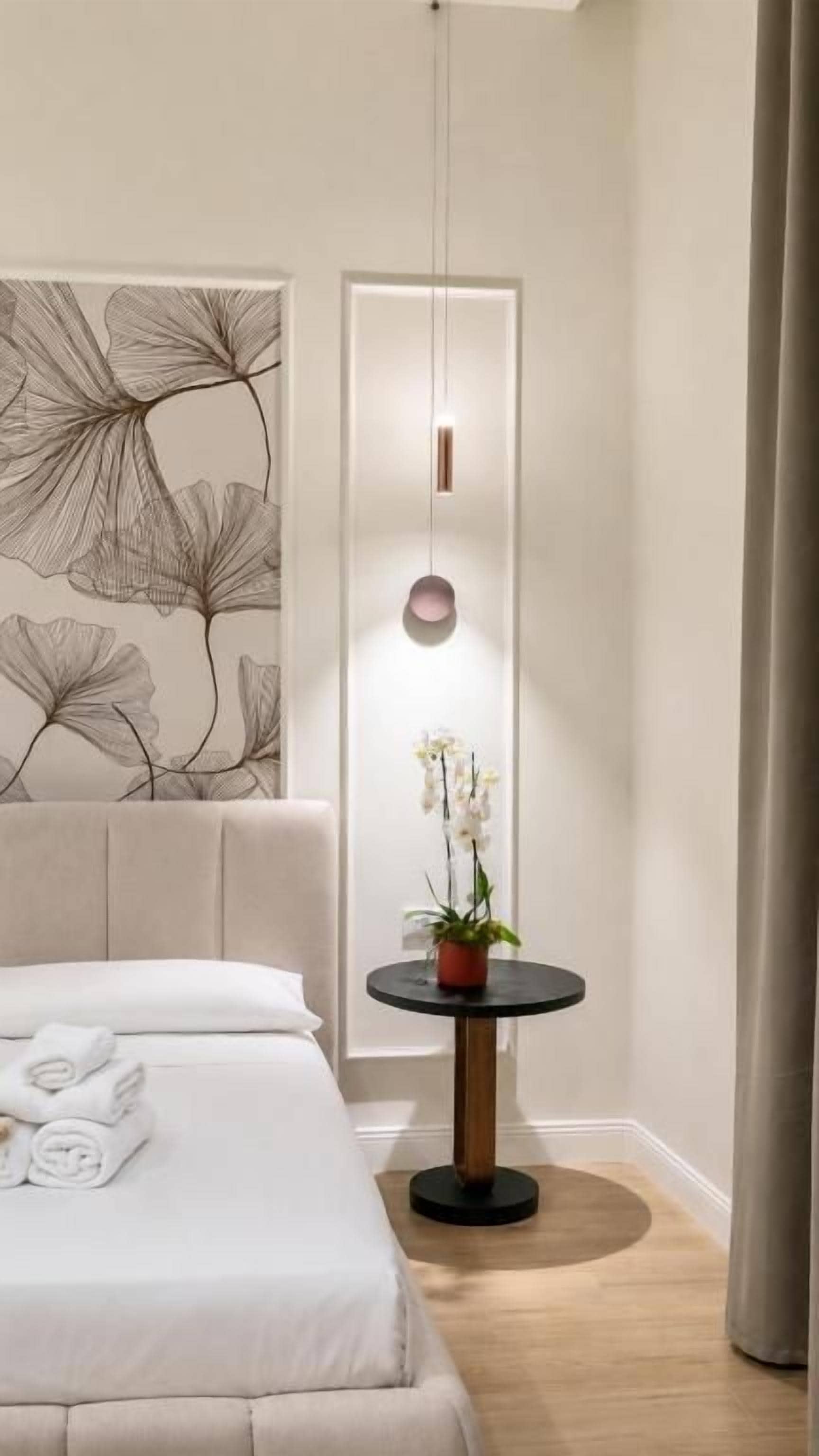 A hotel room with a bed, a round table with a plant, and a wall art piece.