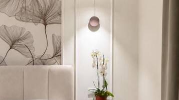 A hotel room with a bed, a round table with a plant, and a wall art piece.
