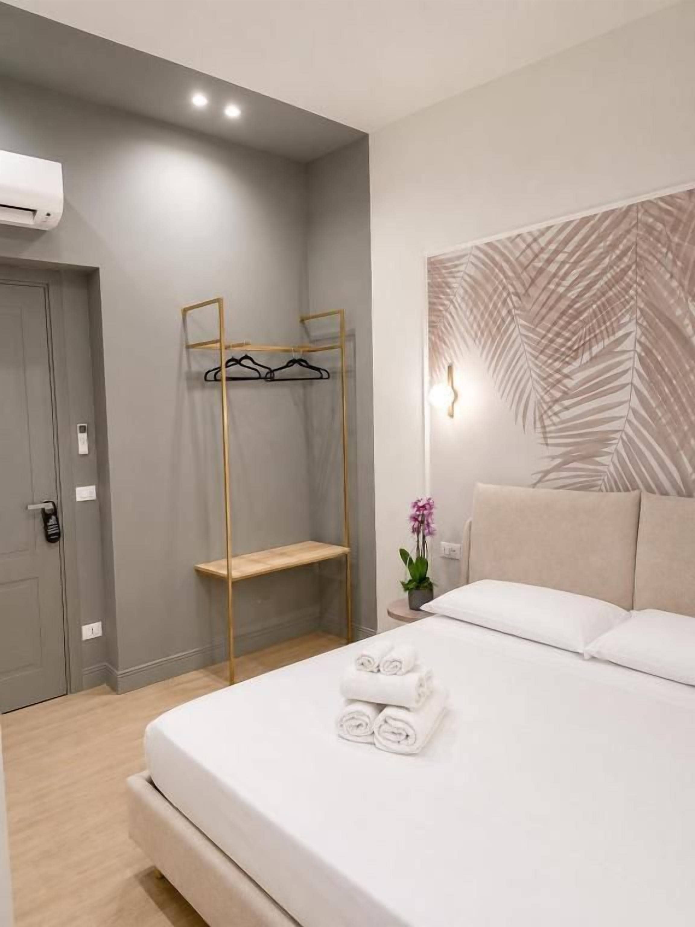 Habitación de hotel moderna con una cama, un banco de madera, perchero en la pared y lámpara de pared.
