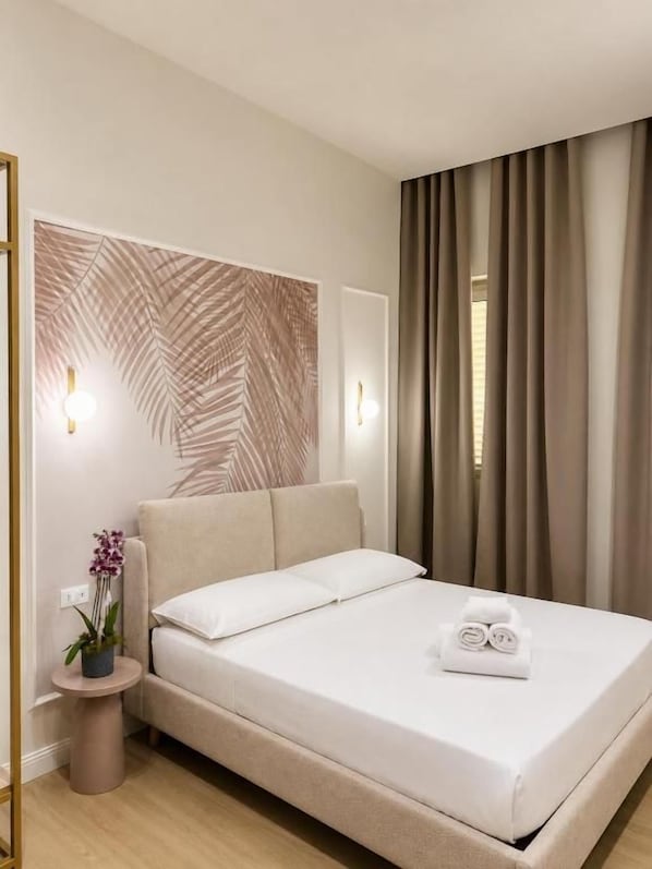 A hotel room with a bed, a wall-mounted light fixture, a potted plant, and a window with curtains. - Xenia Suites Duomo (Reggio Calabria)