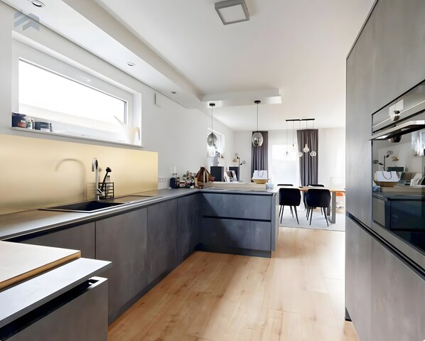 A modern kitchen with a central island, a dining area with chairs, and a large window providing natural light.