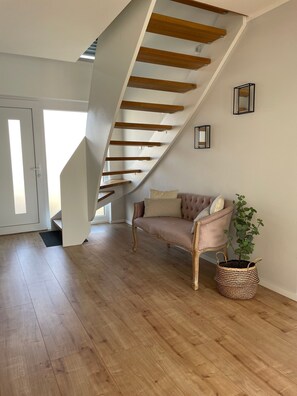 A spacious room with a wooden staircase, a cushioned sofa, and a potted plant.