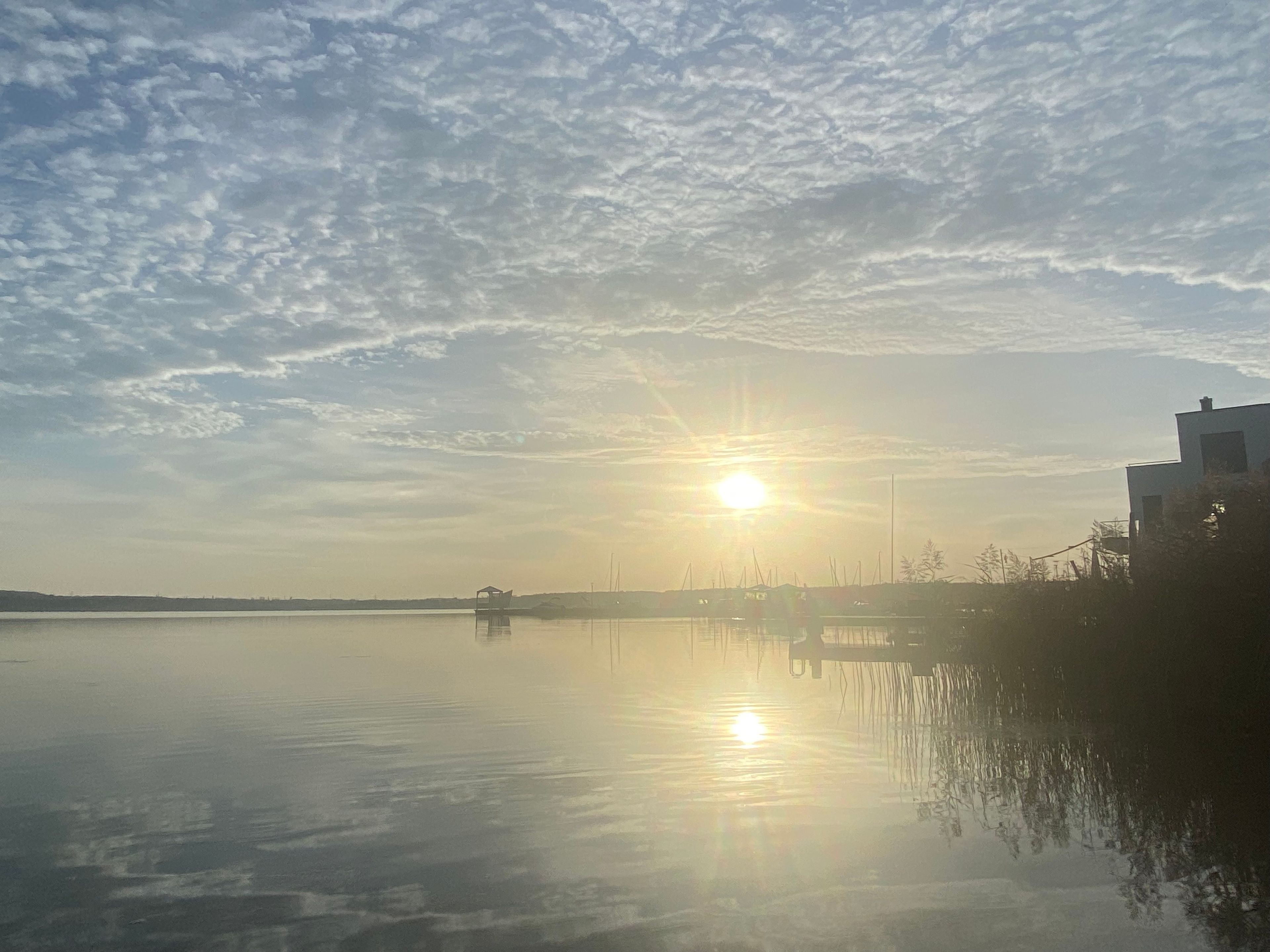 Ruhige Wasseroberfläche spiegelt den Himmel und ein Gebäude mit flachem Dach.