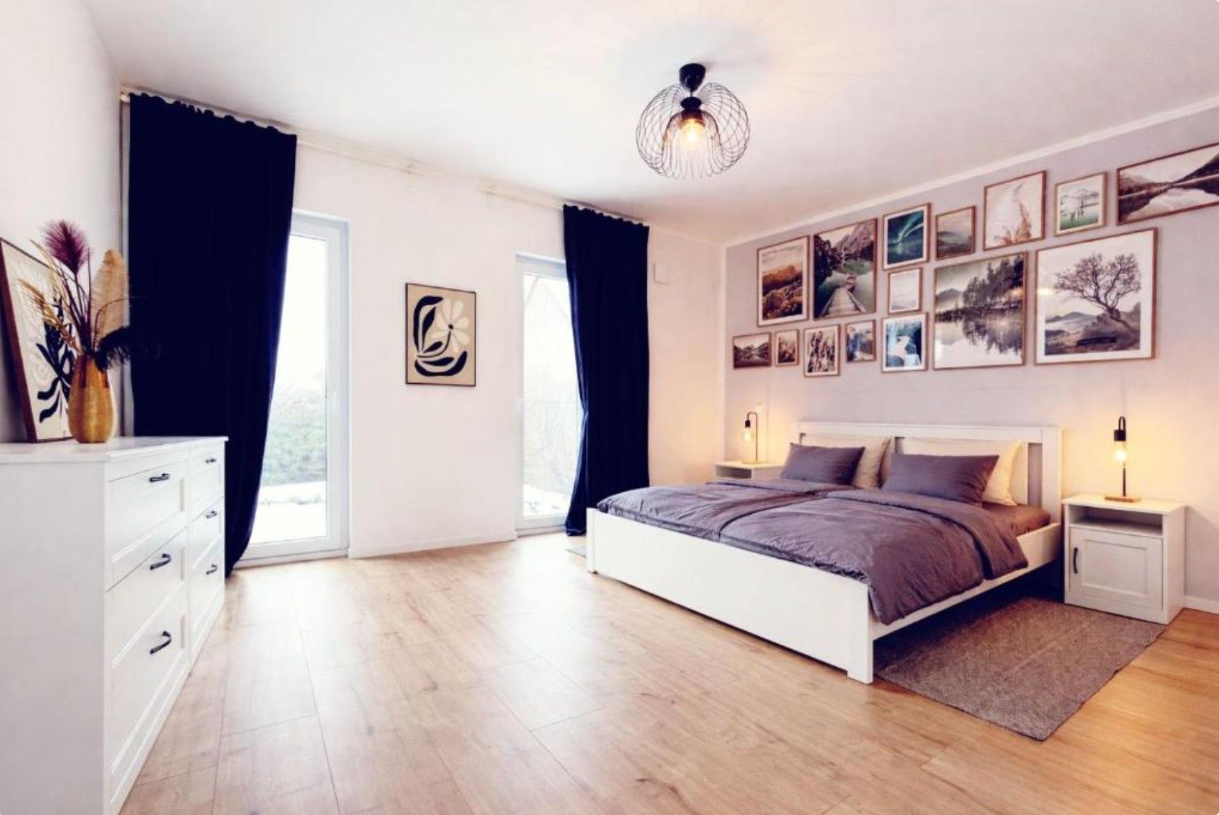 A bedroom with a bed, bedside tables, a dresser, and a large window.