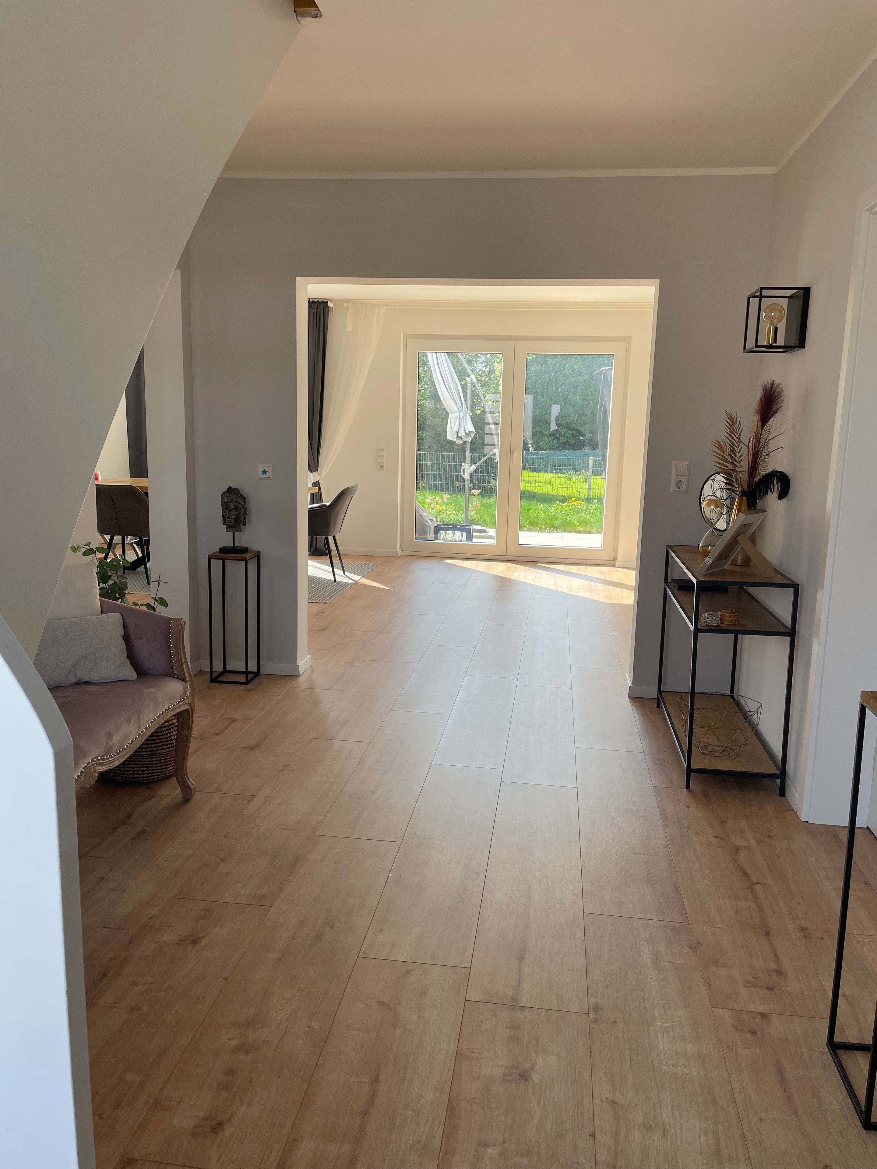 Ein geräumiger Wohnbereich mit einem großen Schiebeglastür, die zu einem Garten führt, eine Couch, ein kleiner Tisch und ein Sessel.