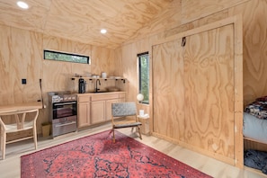 A compact wooden room with a kitchenette, a dining table, a chair, and a bed.