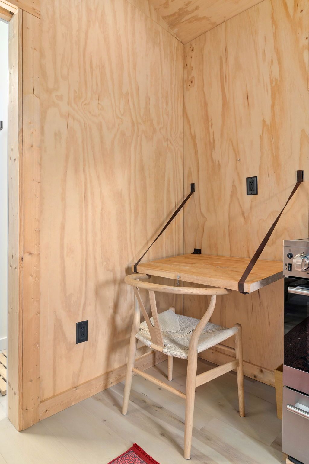 A corner of a room with a wooden wall, a chair with a woven seat, and a metal appliance.