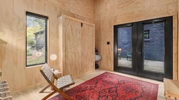 A room with wooden walls, a large window, a sliding door, a red patterned rug, and a chair.