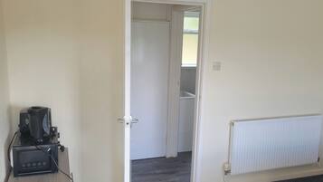Una habitación con un radiador blanco, una puerta cerrada y una cafetera sobre un pedestal.
