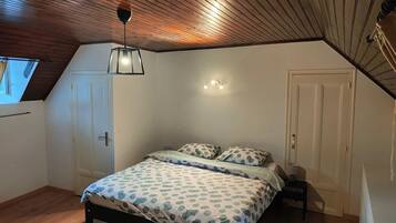 A bedroom with a sloped ceiling, a bed with patterned bedding, a bedside table, and a wall-mounted light fixture.