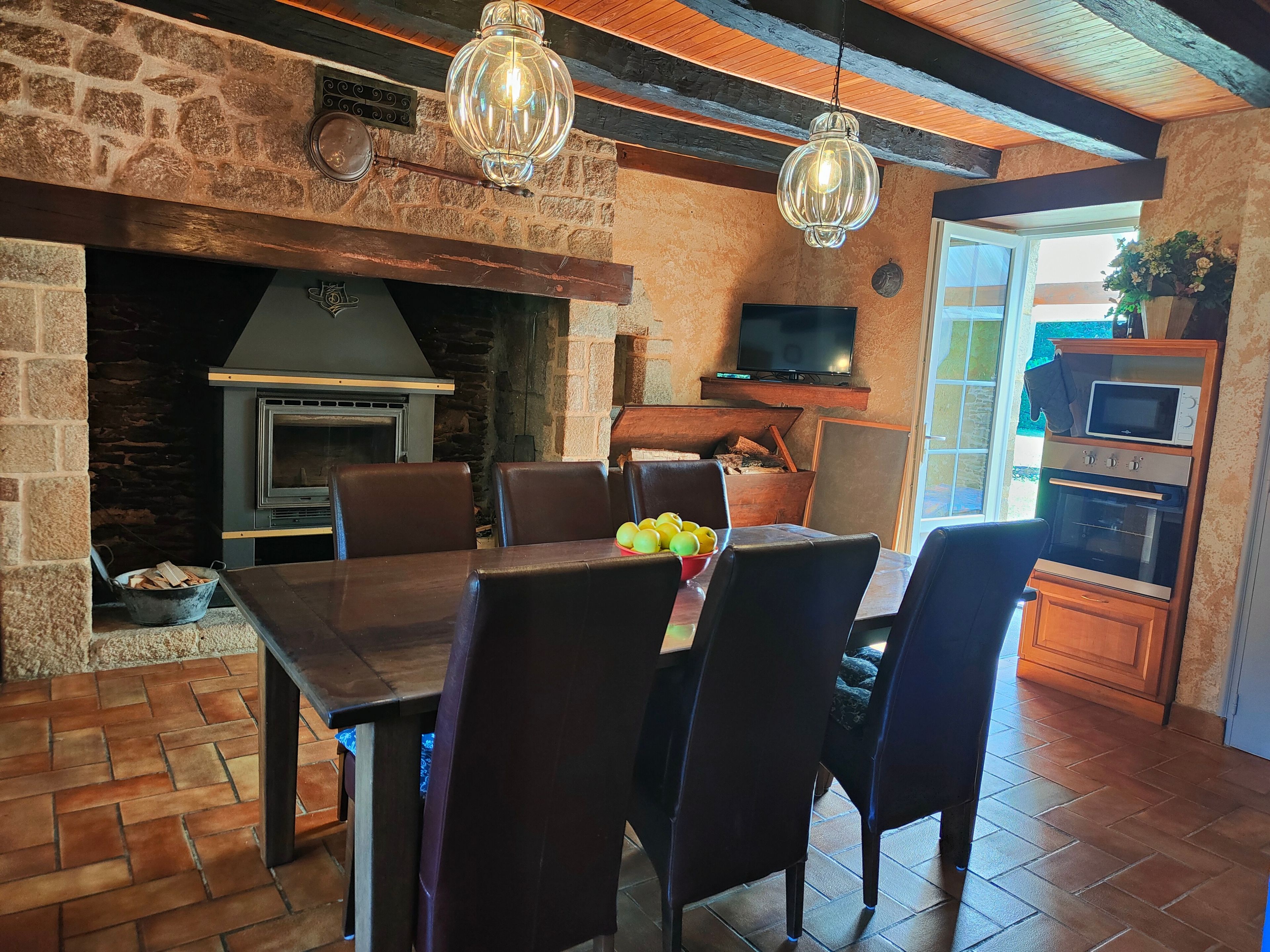 Een landelijke inrichting met een stenen openhaard, houten balken in het plafond, een eettafel met stoelen en een keuken met inbouwapparatuur.