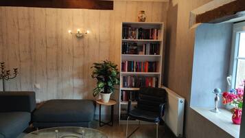 A cozy living room with a bookshelf, a black chair, a glass coffee table, and a potted plant.