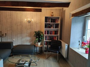 Een gezellige woonkamer met een boekenkast, een zwarte fauteuil, een glazen salontafel en een potplant.