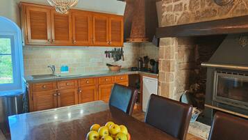 Una cocina con armarios de madera, pared de piedra, horno empotrado y mesa de comedor con sillas.