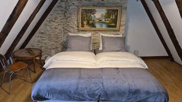 A bedroom with a loft bed, a painting on the wall, a small round table, and a chair.