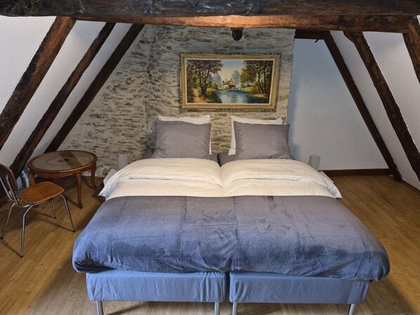 Een slaapkamer met een hoogslaper, een schilderij aan de muur, een klein rond tafeltje en een stoel.