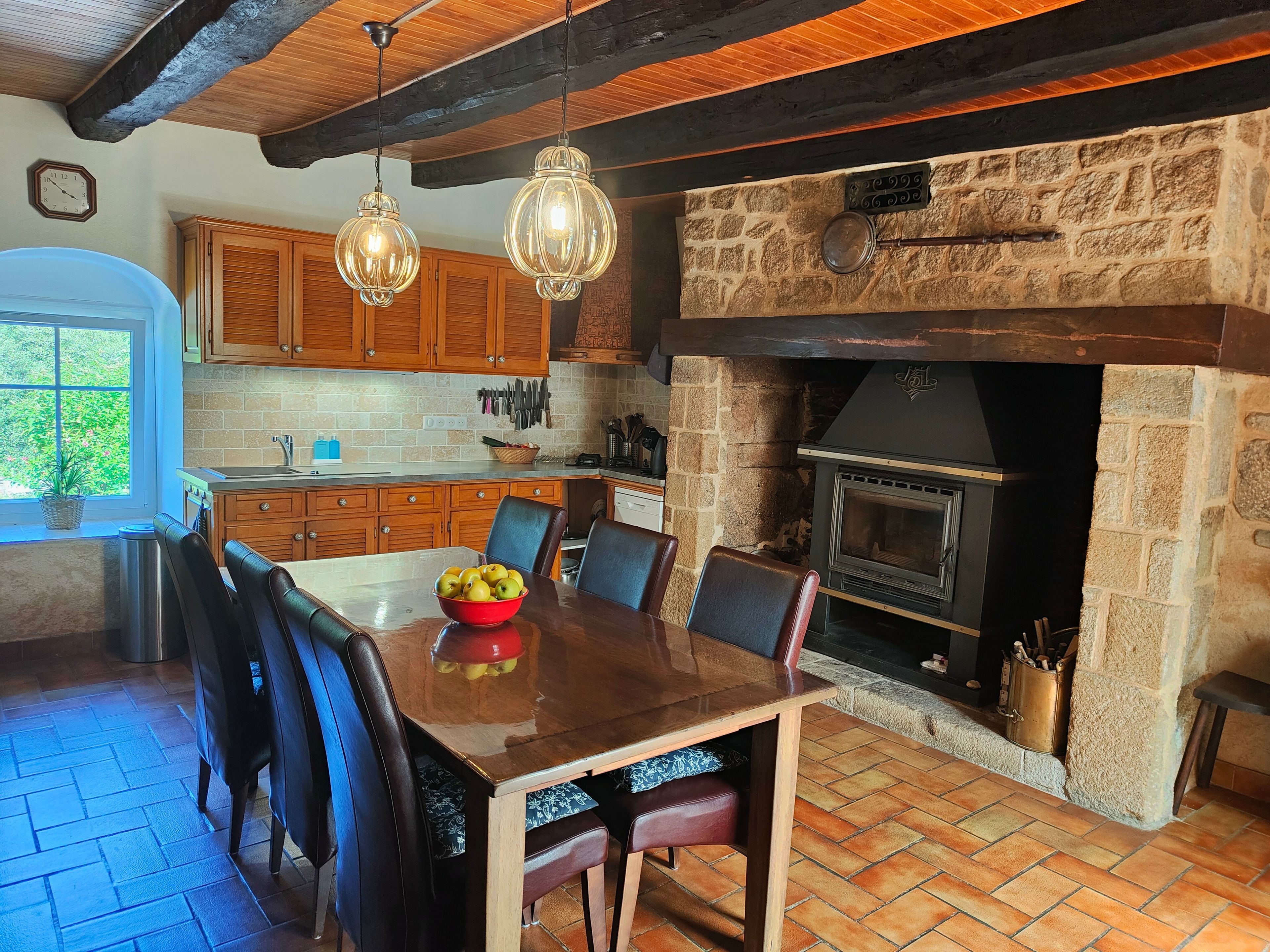 A rustic kitchen with a stone fireplace, wooden cabinets, and a dining table with chairs.
