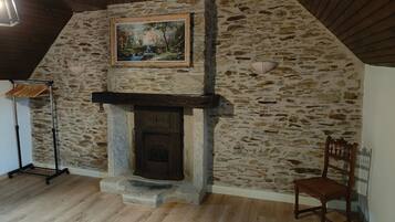 A room with a stone wall, a fireplace, a wooden chair, and a painting.