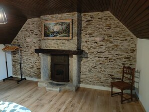 Una habitación con pared de piedra, chimenea, una silla de madera y un cuadro.