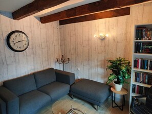Ein Wohnzimmer mit einer Couch, einer Wanduhr, einem Bücherregal und einer Zimmerpflanze.