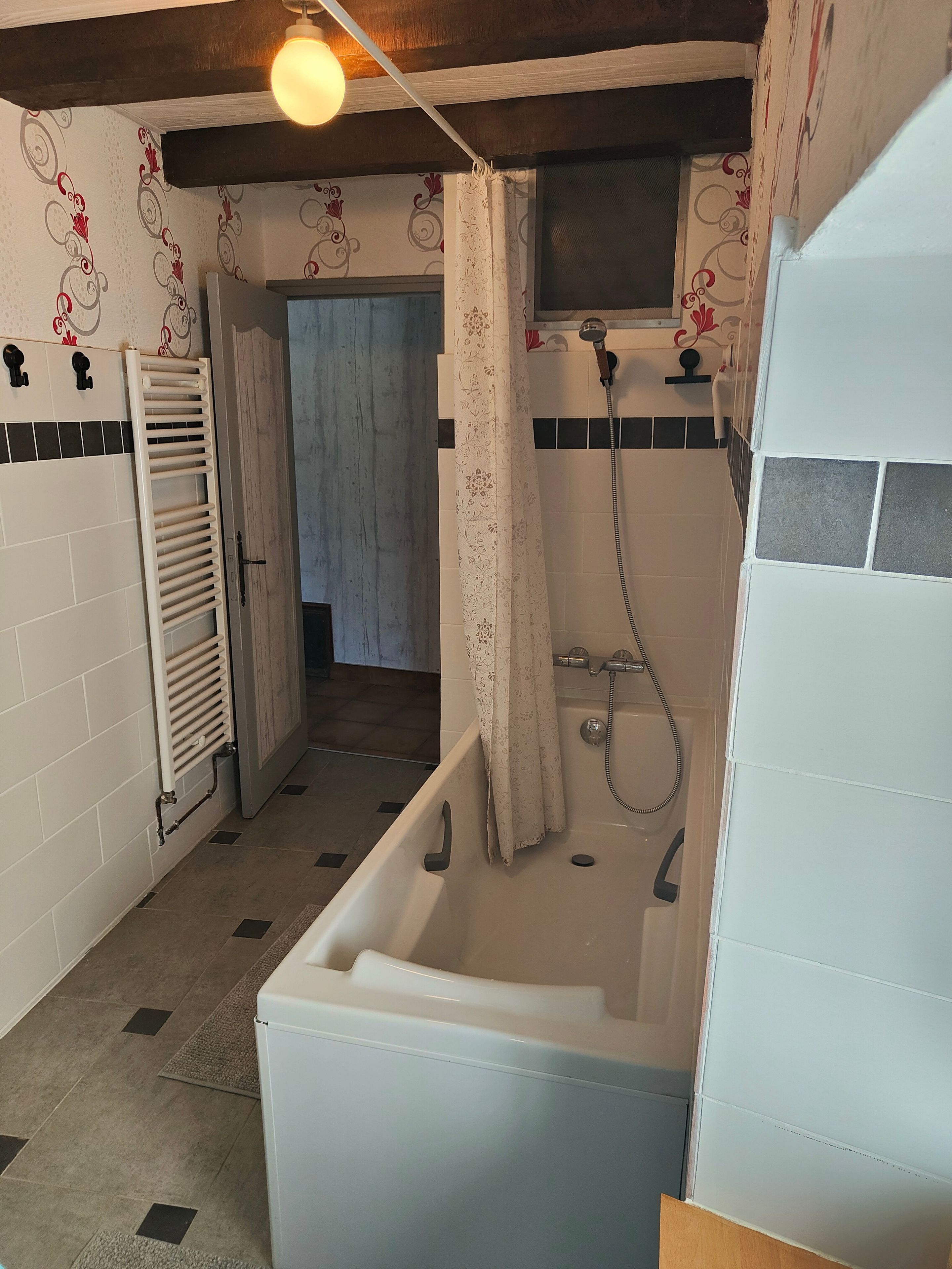 Een badkamer met een badkuip, douche, betegelde wanden en een hanglamp.