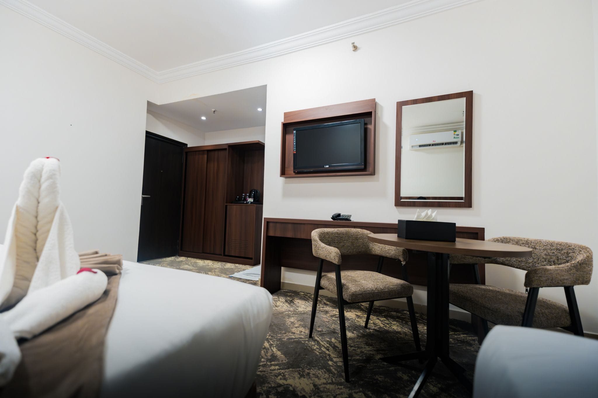 A hotel room with a bed, a desk with two chairs, a television, and a mirror.