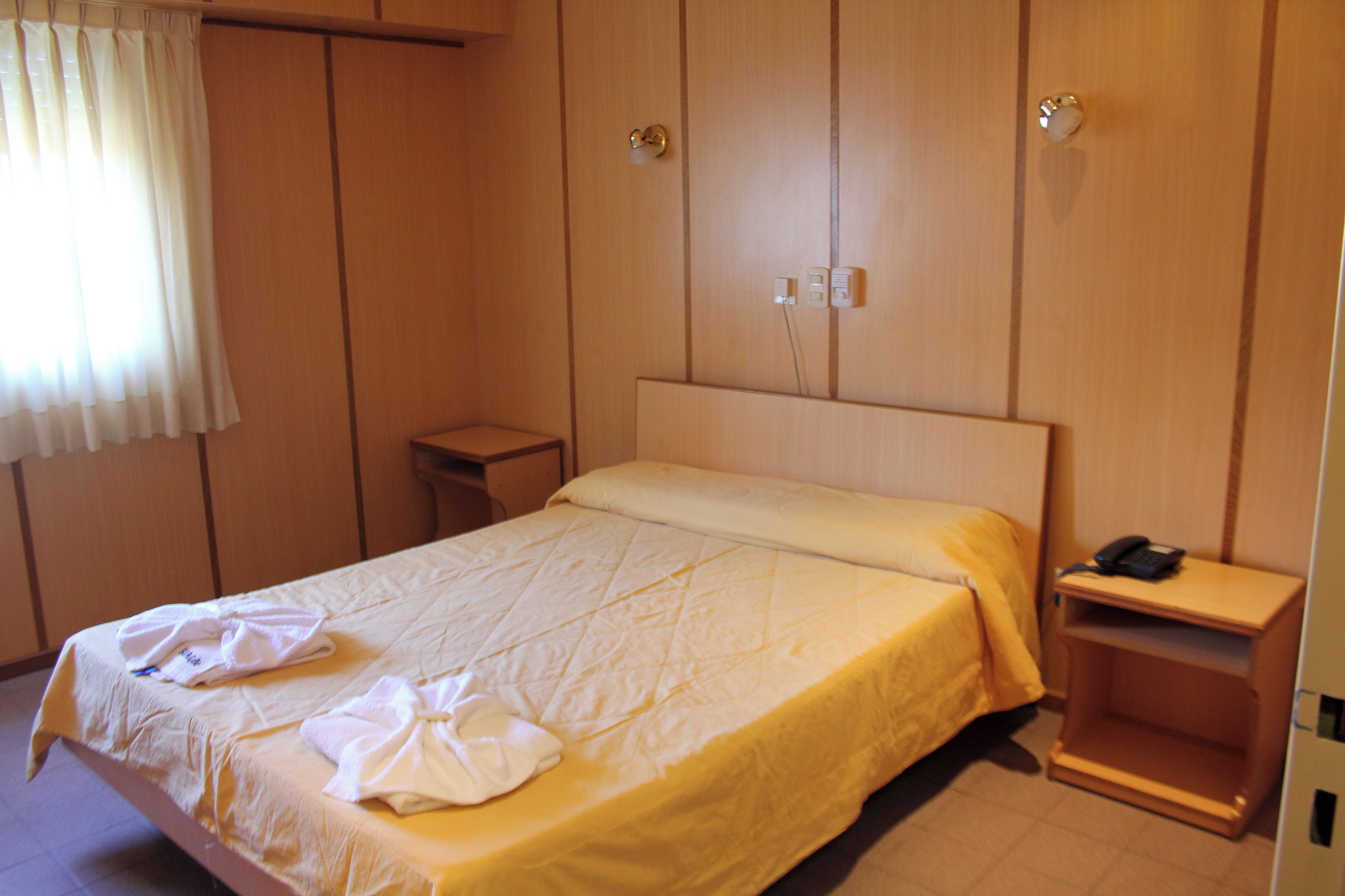 A hotel room with a bed, a bedside table with a phone, and a wardrobe with a mirror.