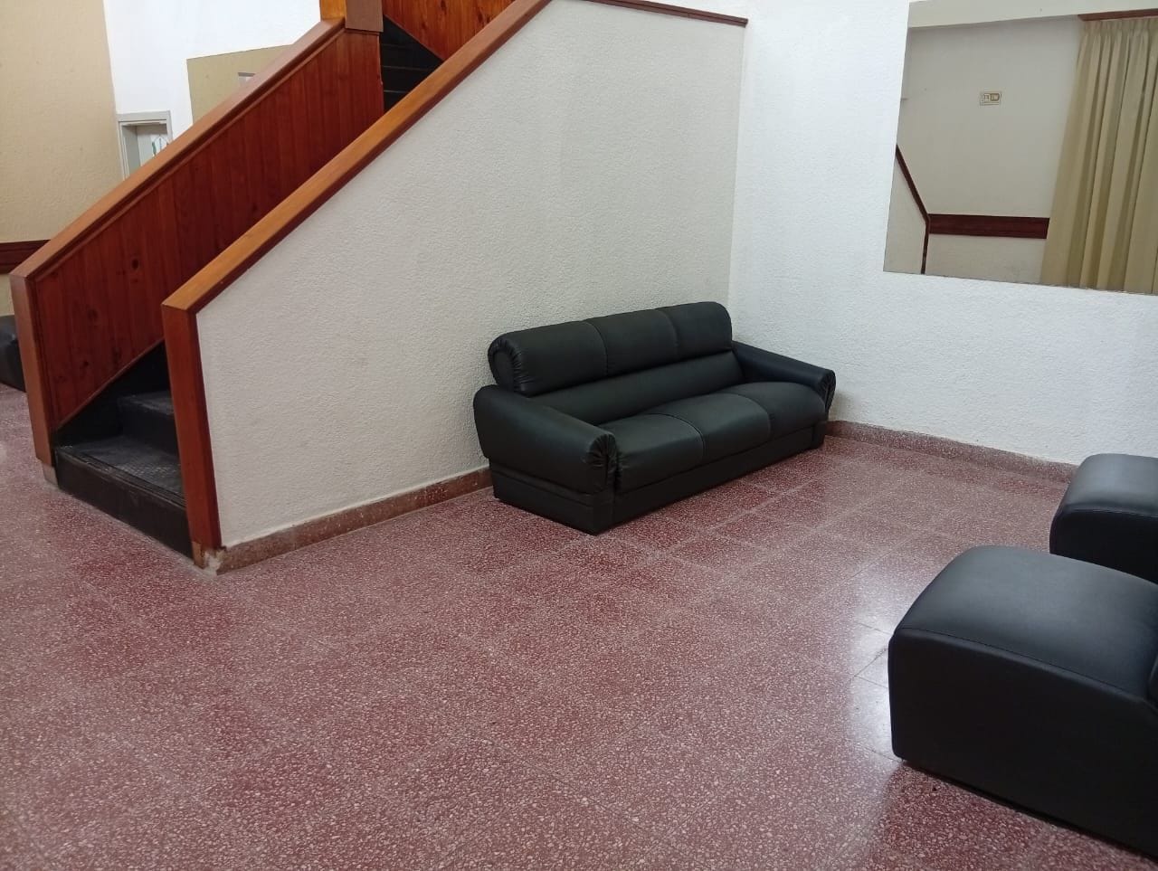 A room with a staircase, a black sofa, and a red speckled floor.