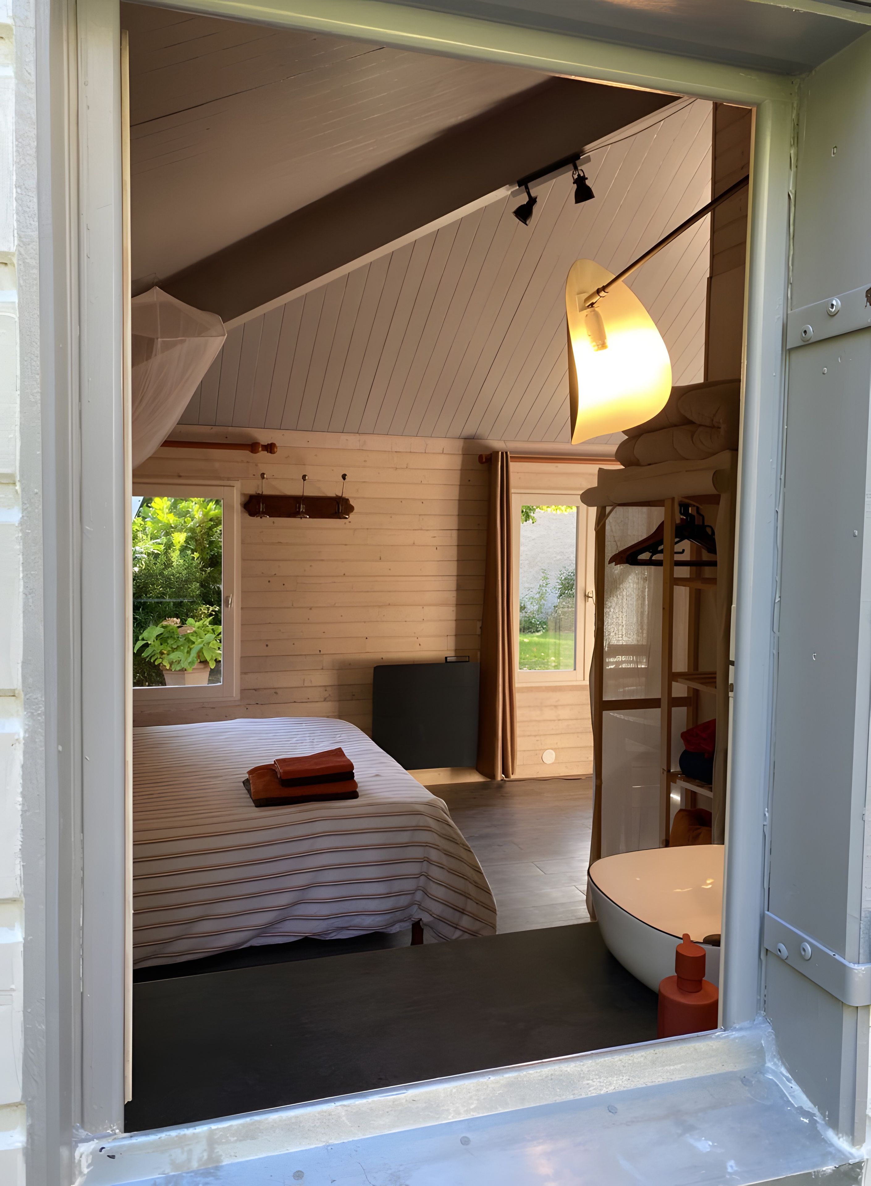 Une pièce comprenant un lit, un bureau, une chaise, un luminaire suspendu et donnant sur l’extérieur.