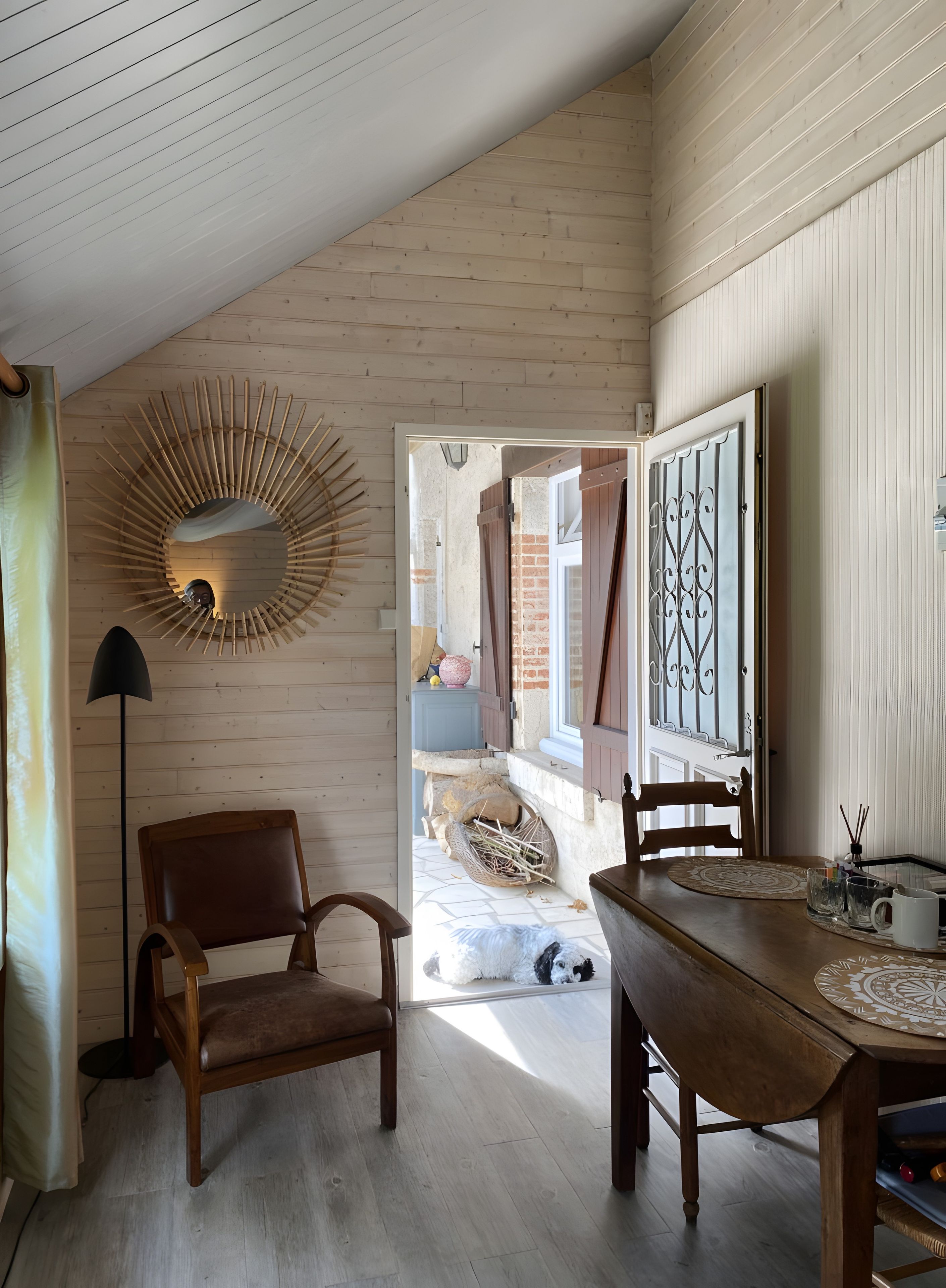 Une pièce avec un plancher en bois, une table à manger avec des chaises, une lampe et un miroir décoratif.