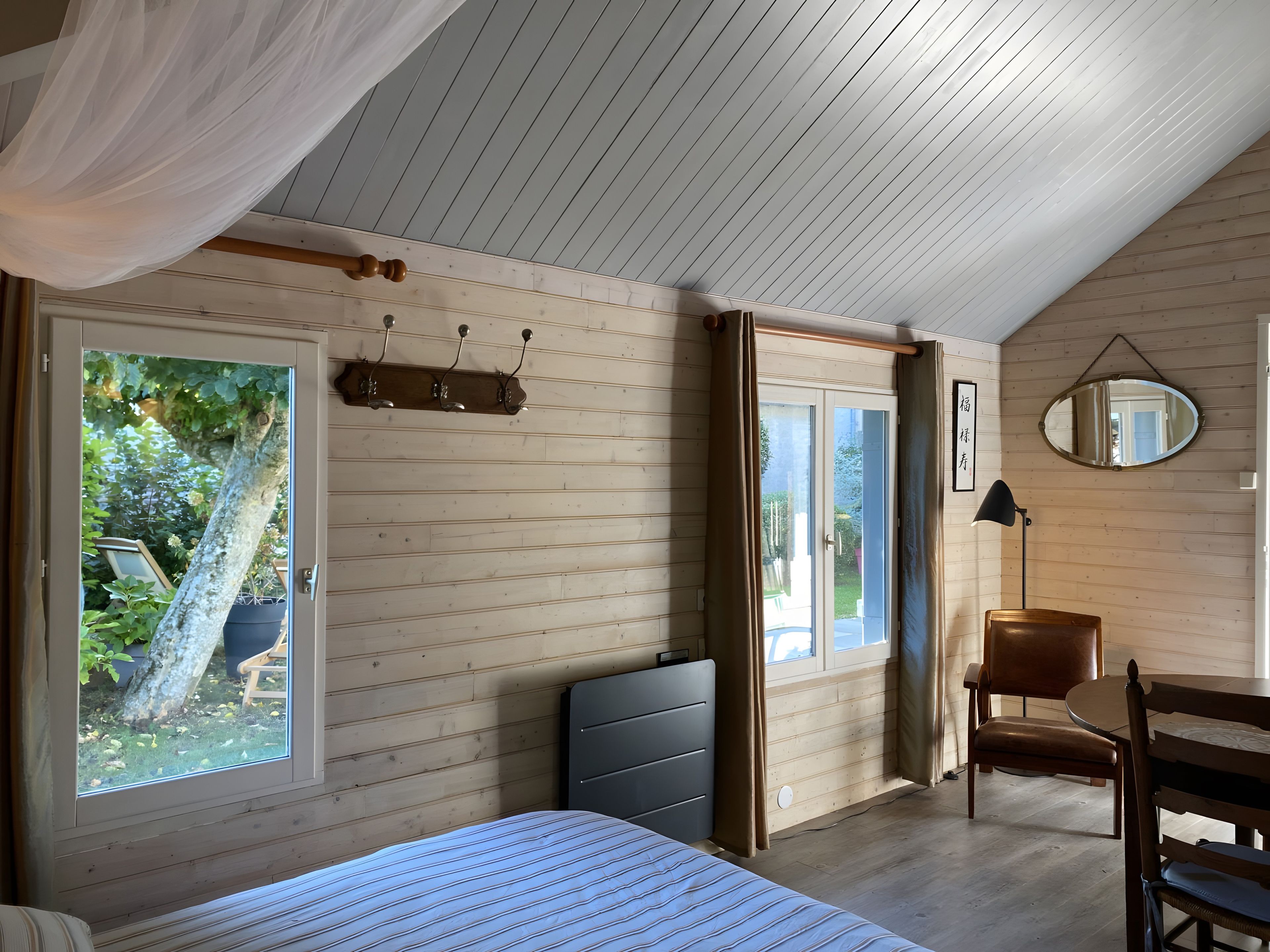 Une chambre à coucher avec un lit, une chaise, un bureau, un miroir et une fenêtre avec des rideaux.