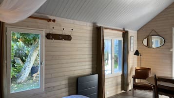 A bedroom with a bed, a chair, a desk, a mirror, and a window with curtains.