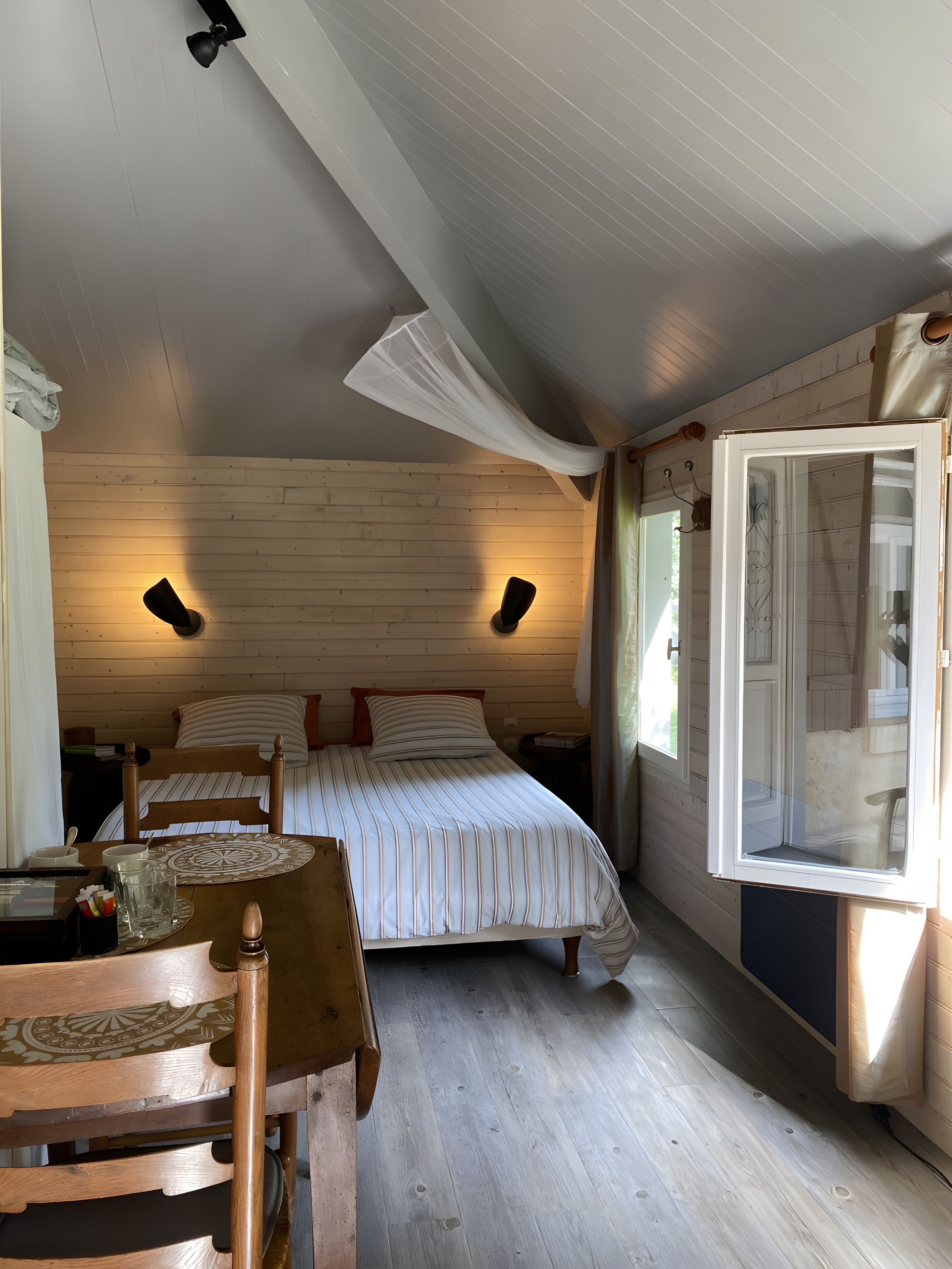 Un dormitorio con cama, mesitas de noche, suelo de madera y una ventana con cortinas.