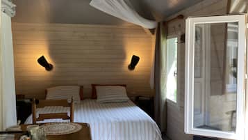 Un dormitorio con cama, mesitas de noche, suelo de madera y una ventana con cortinas.