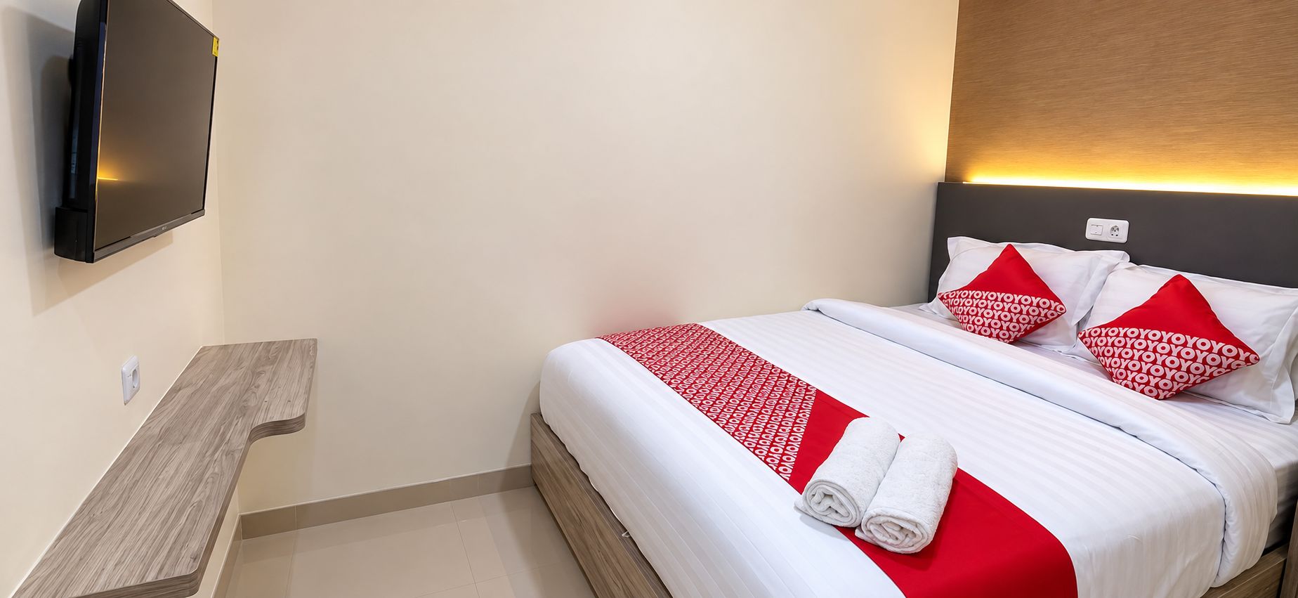 Ein Hotelzimmer mit einem Bett, einem flachbildfernseher an der Wand und einem Nachttisch aus Holz.