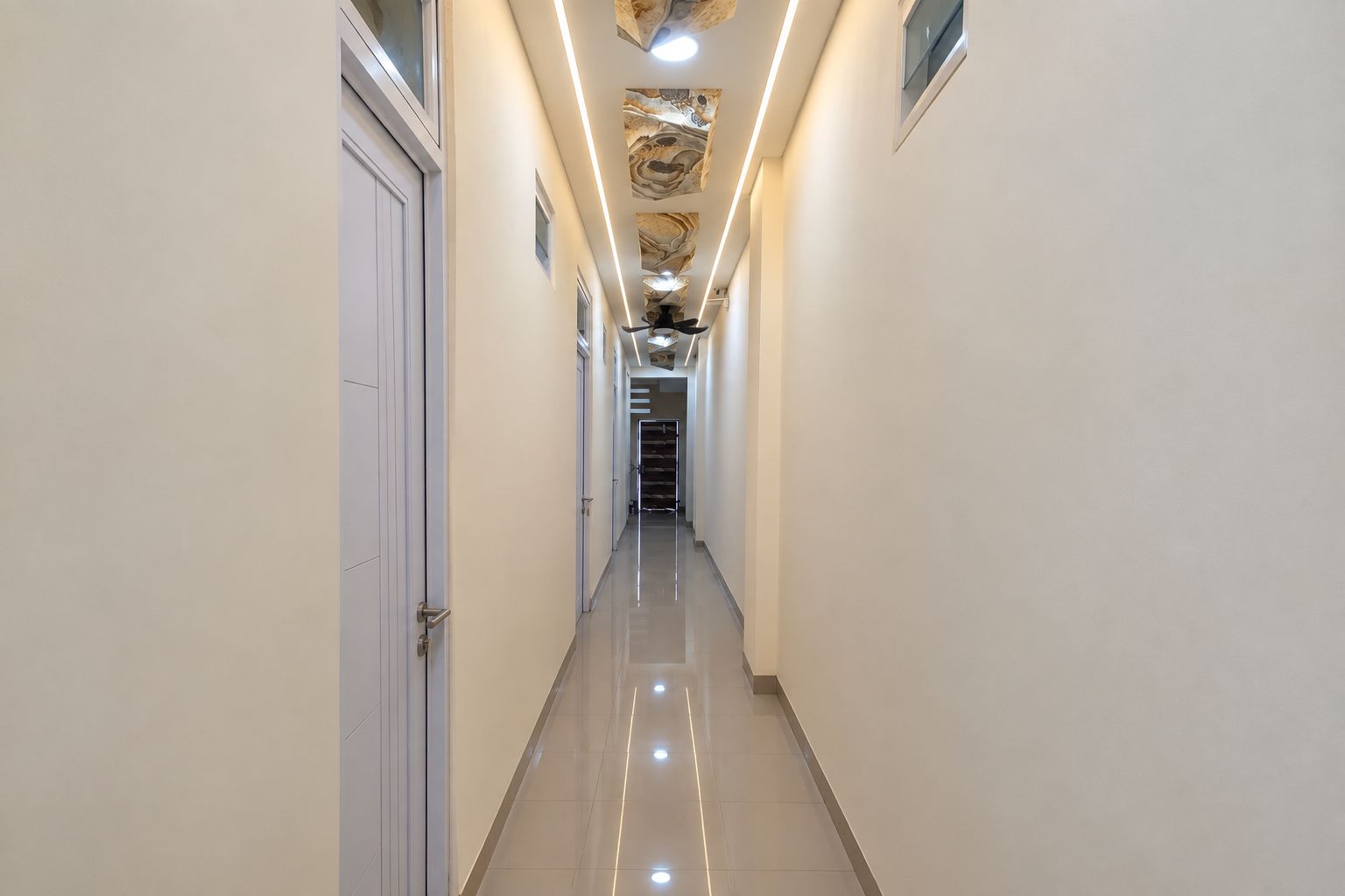 Un pasillo largo y estrecho con piso brillante, paredes blancas y techo con un diseño decorativo.