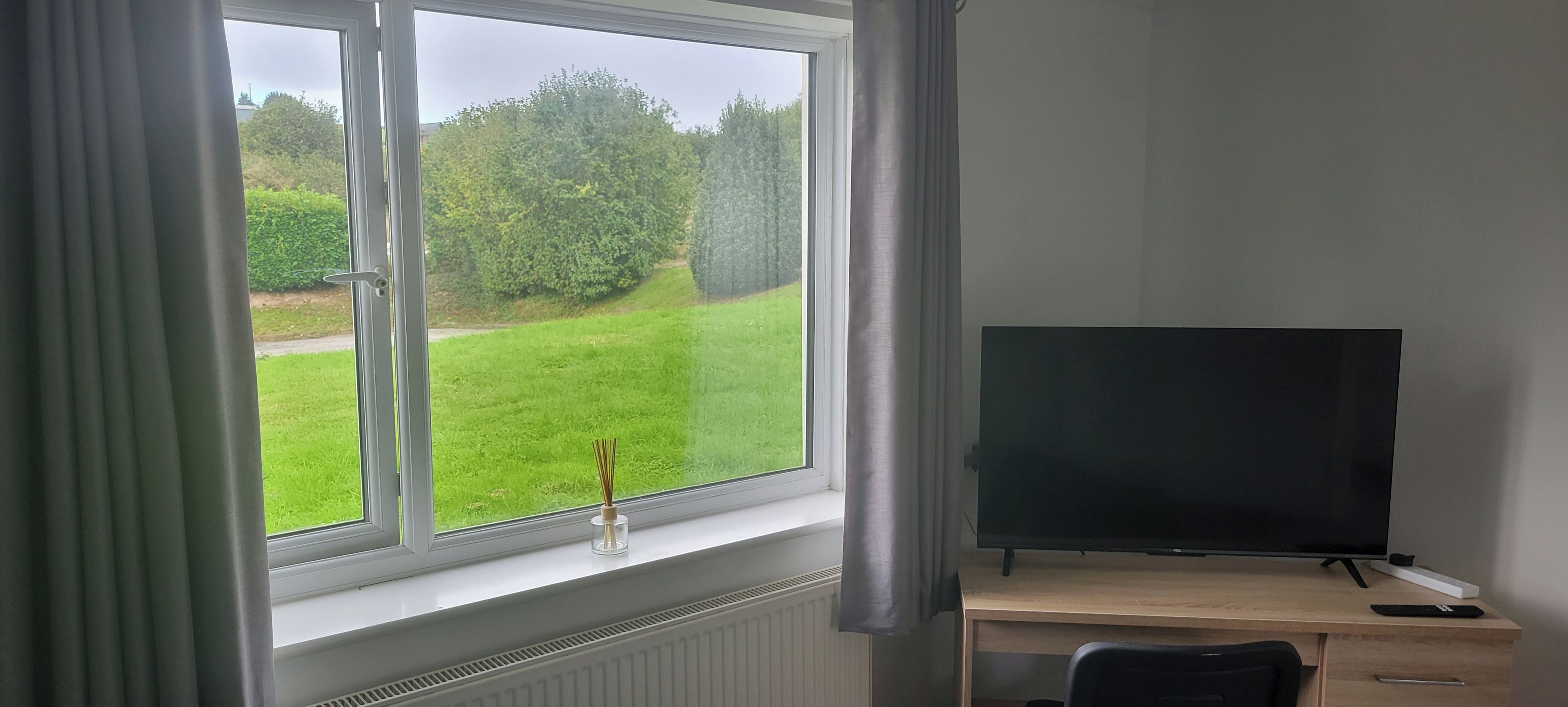Una habitación con un ventanal grande, un escritorio, una silla y un televisor.