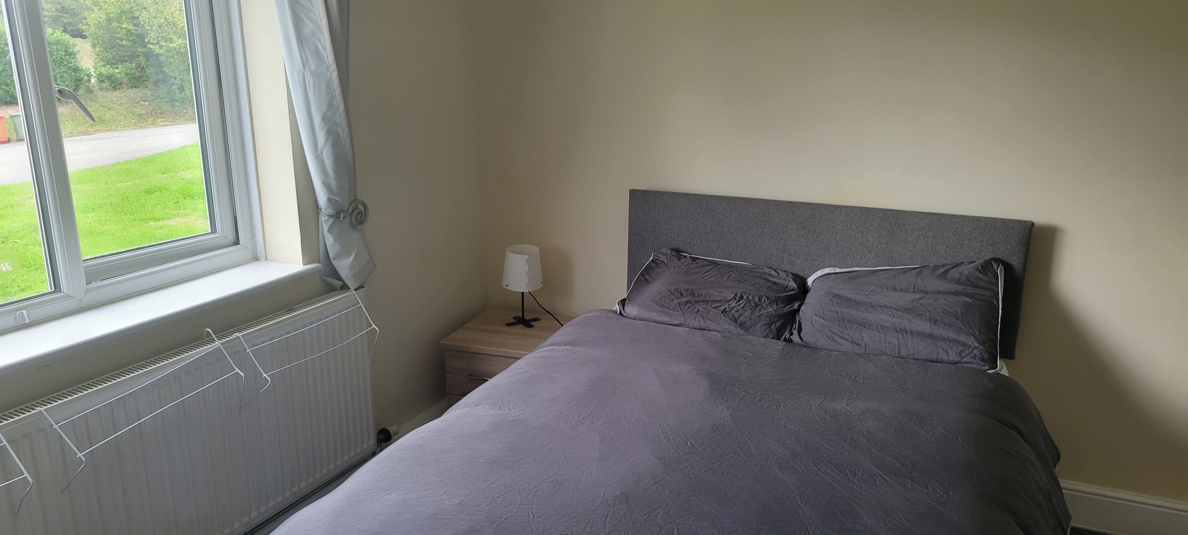 Un dormitorio con una cama, una mesita de noche, una lámpara y una ventana con cortinas.