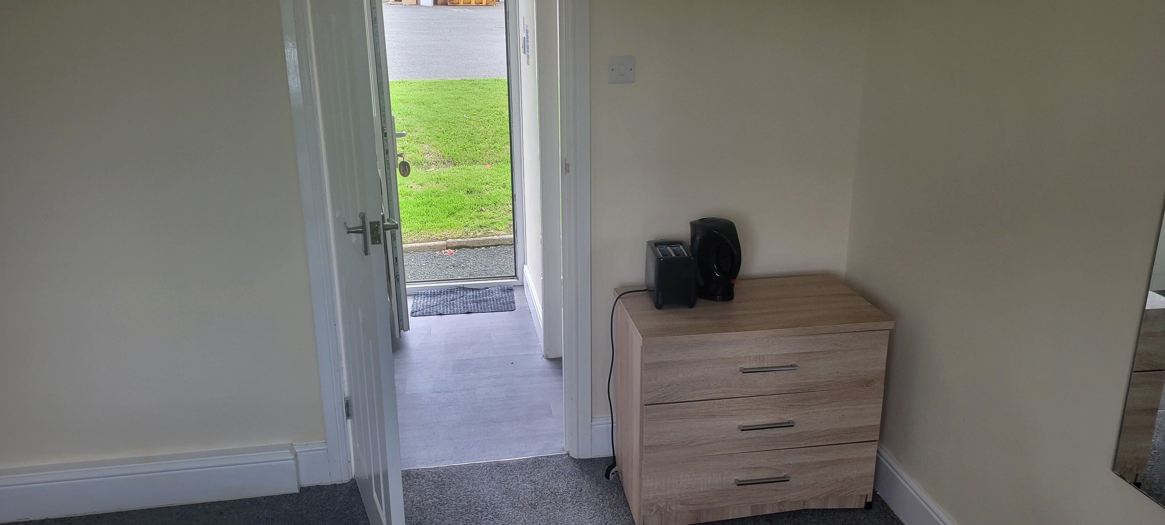 Una habitación con un aparador de madera, una puerta que da al exterior y una pequeña alfombra en el suelo.