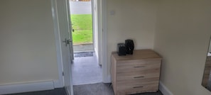 Quarto com cômoda de madeira, porta que dá para o exterior e pequeno tapete no chão.