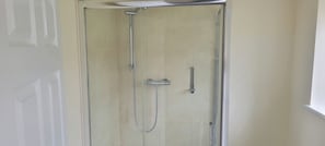 Box de vidro com chuveiro manual e torneira fixa na parede.