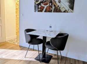 Un pequeño comedor con una mesa y dos sillas, una botella de agua sobre la mesa y una obra de arte colgada en la pared.