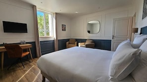 Habitación de hotel con cama, escritorio, silla, televisor, ventana y puerta.