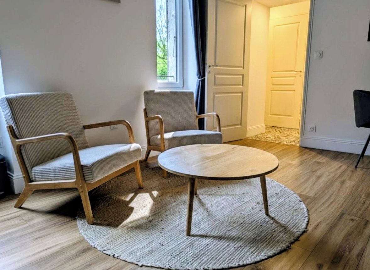 Une pièce avec une table ronde en bois, deux fauteuils rembourrés, un tapis tissé et un plancher en bois.