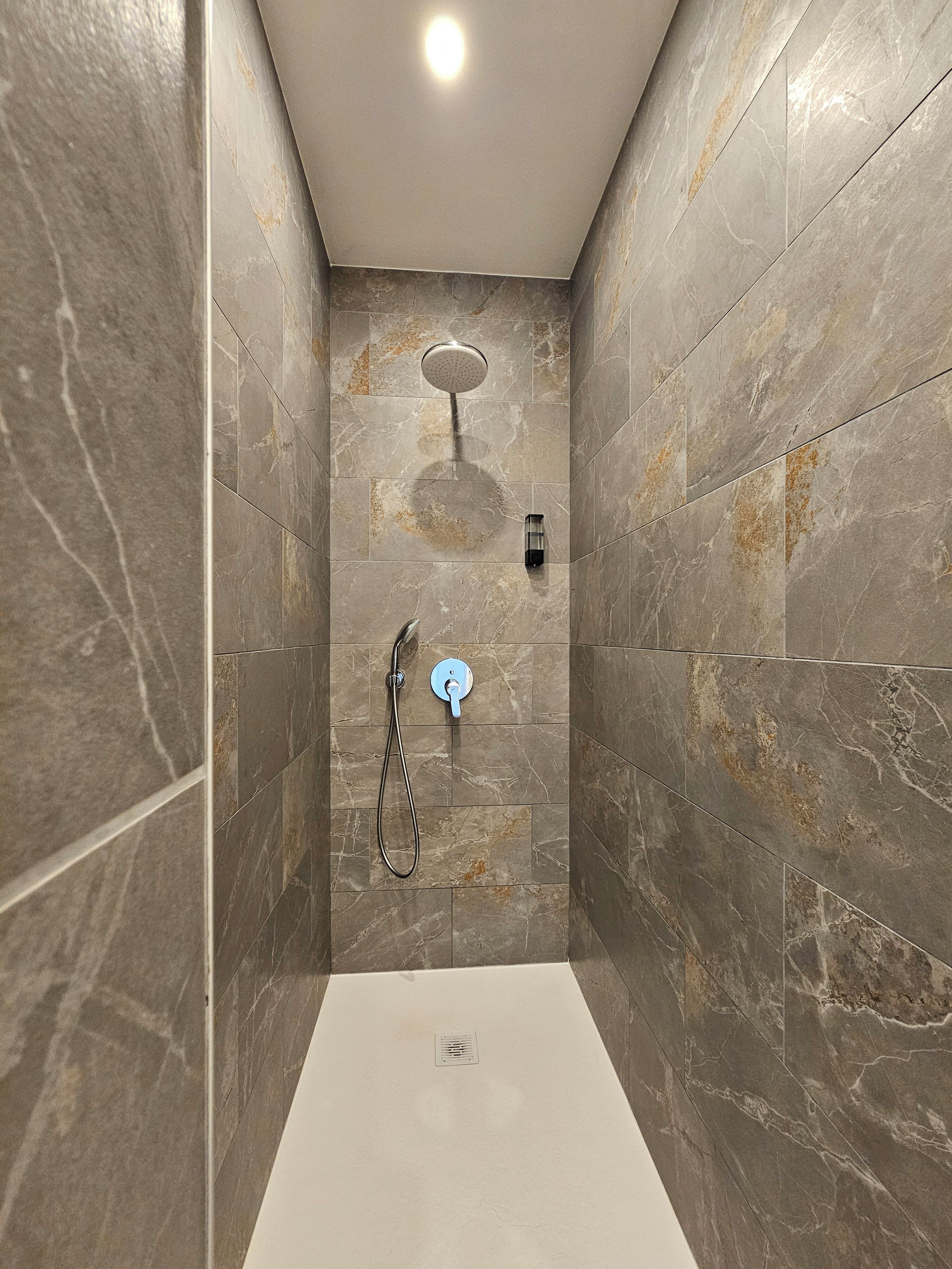 Een moderne douche met een handdouche en een bediening aan de muur.