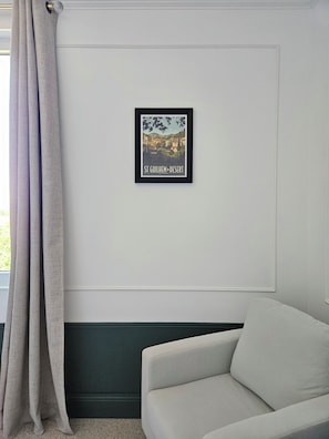 A framed picture of St. Gulik Desert on a white wall, a grey sofa, and a window with grey curtains.