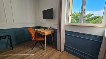 Een hoekkamer met een houten tafel en stoel, een flatscreen televisie aan de muur en een raam met uitzicht op groen.