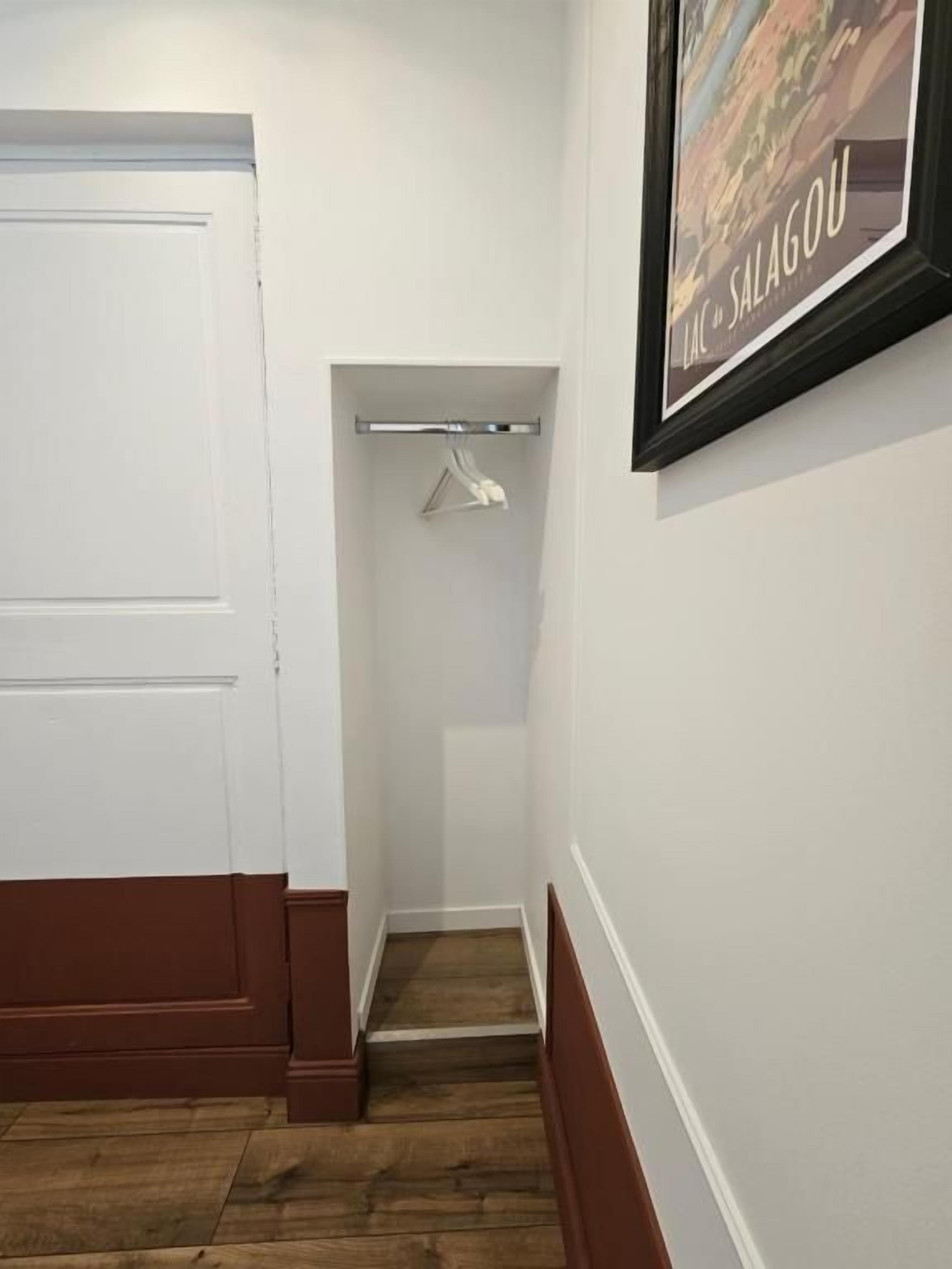 Un pasillo con una puerta blanca, un perchero y un cuadro en la pared.