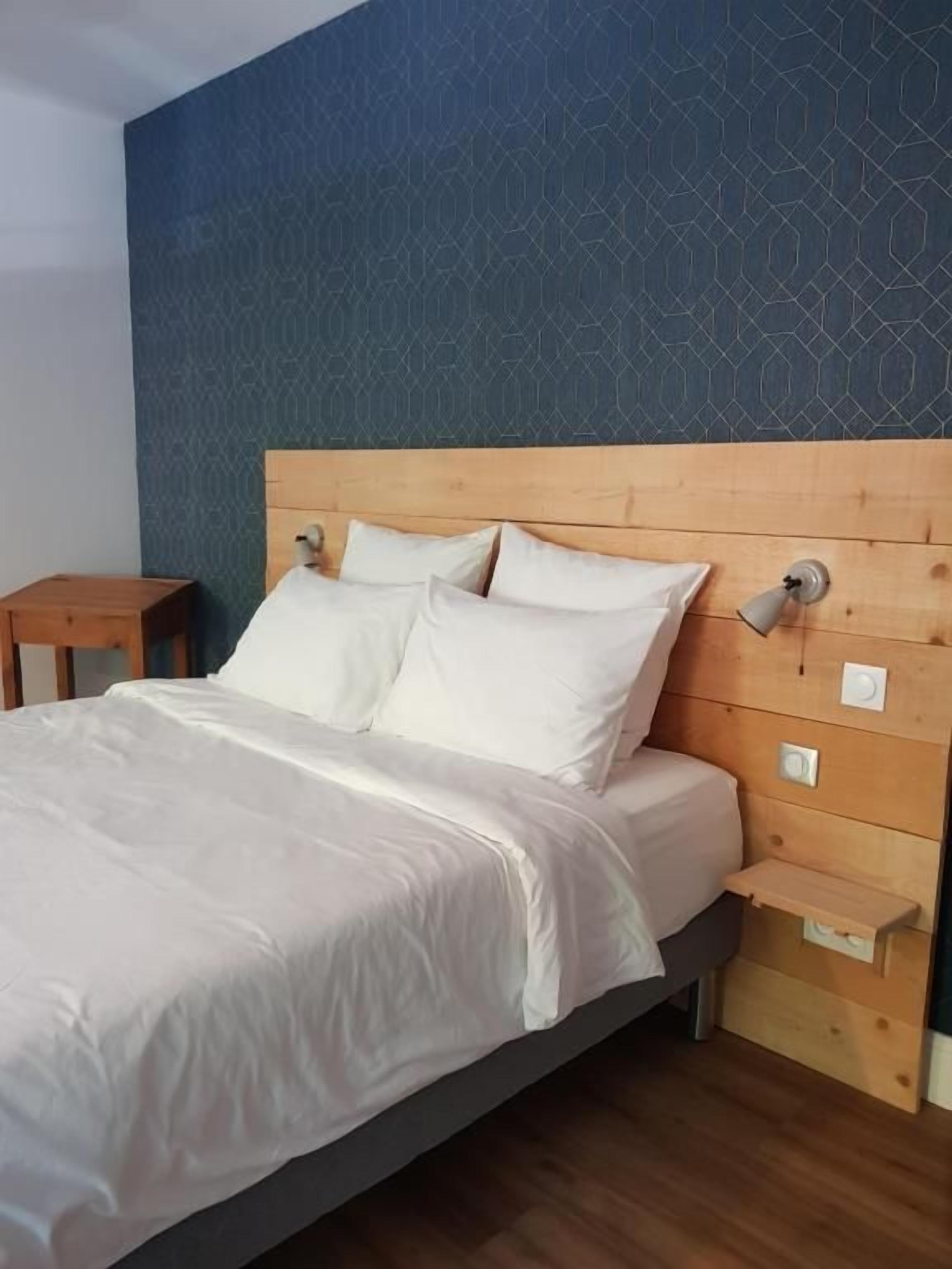 Een bed met witte beddengoed, een houten hoofdbord en een nachtkastje met een lamp.