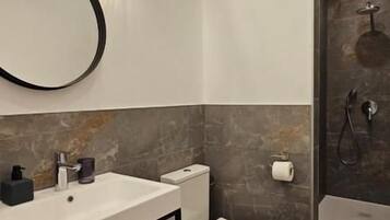 Une salle de bain moderne avec un lavabo, des toilettes et une zone de douche, le tout de couleur blanche.